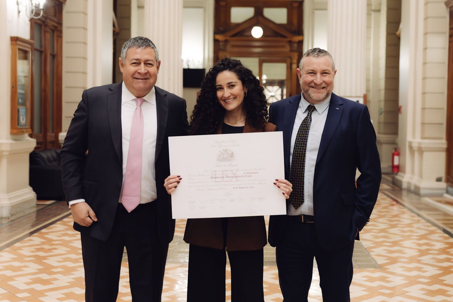 Three men pose with an official certificate in a grand hallway.