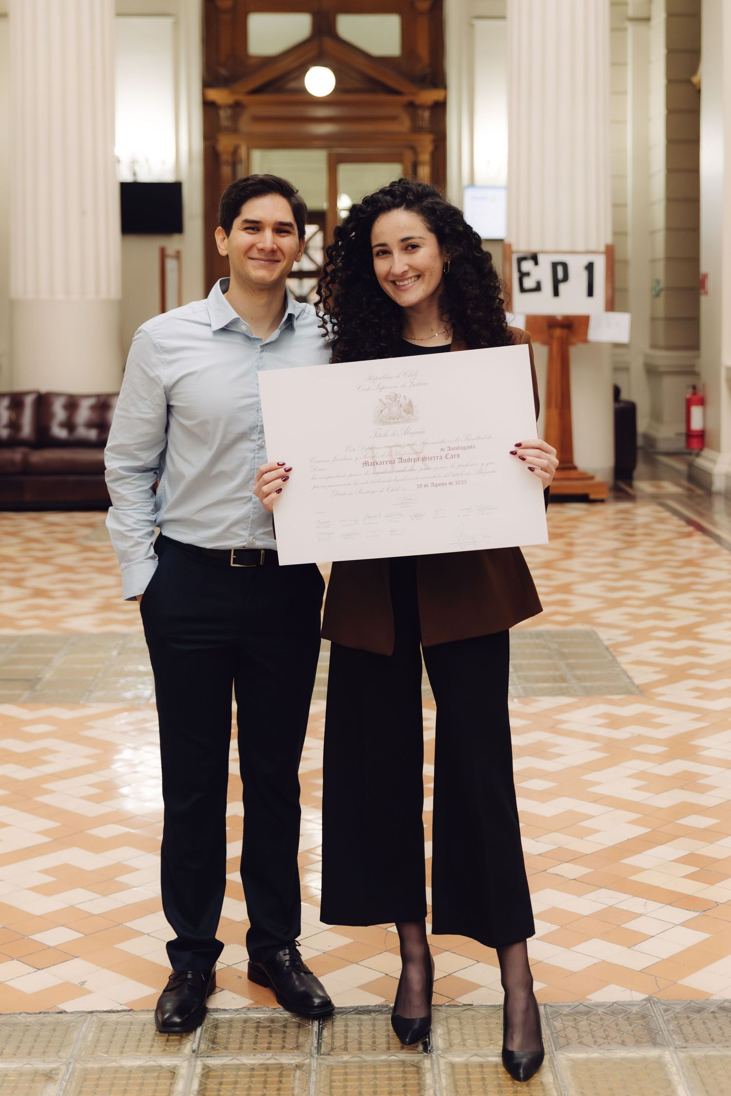 Man and woman proudly holding a diploma certificate in an elegant hall.