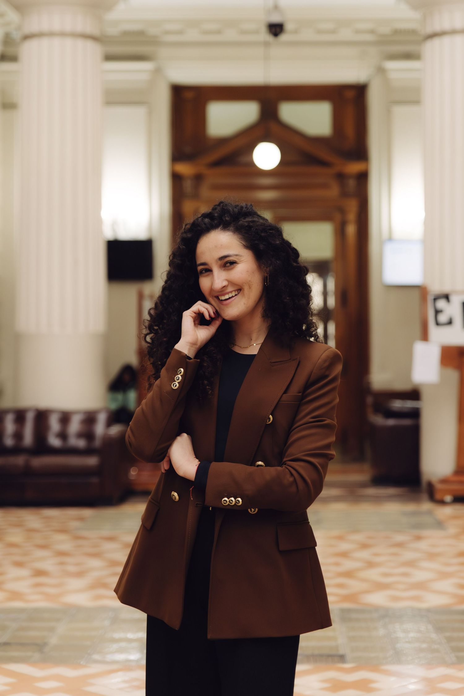 Happy woman in brown blazer laughing in a grand architectural interior.