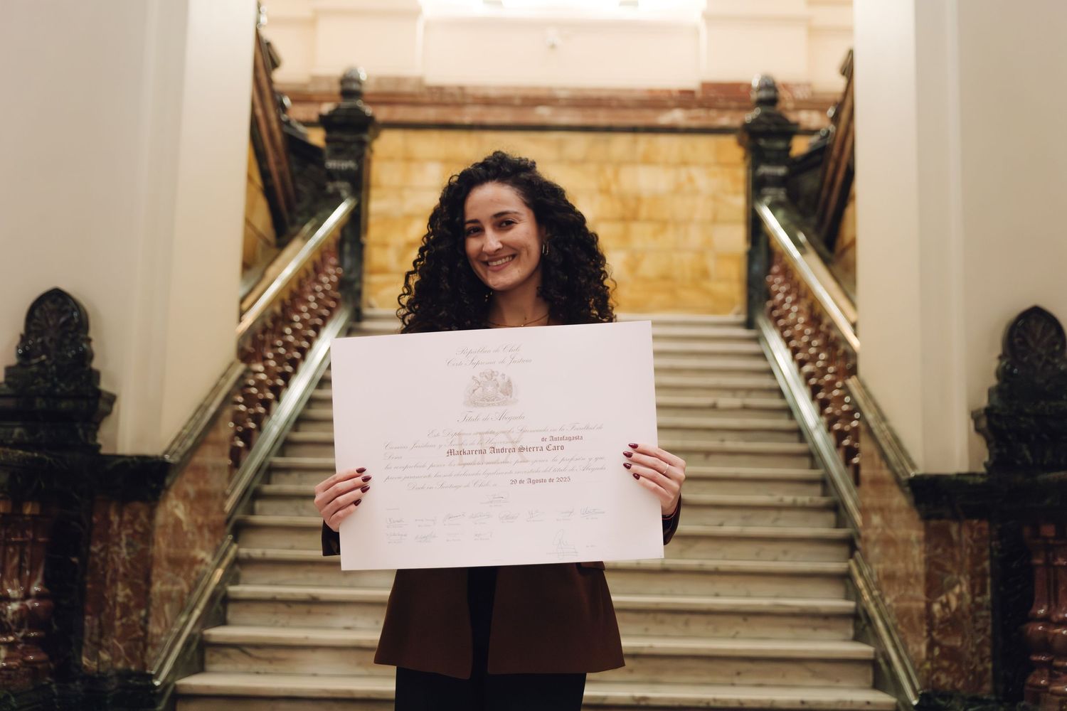 Young woman proudly holding a diploma certificate on a grand staircase.