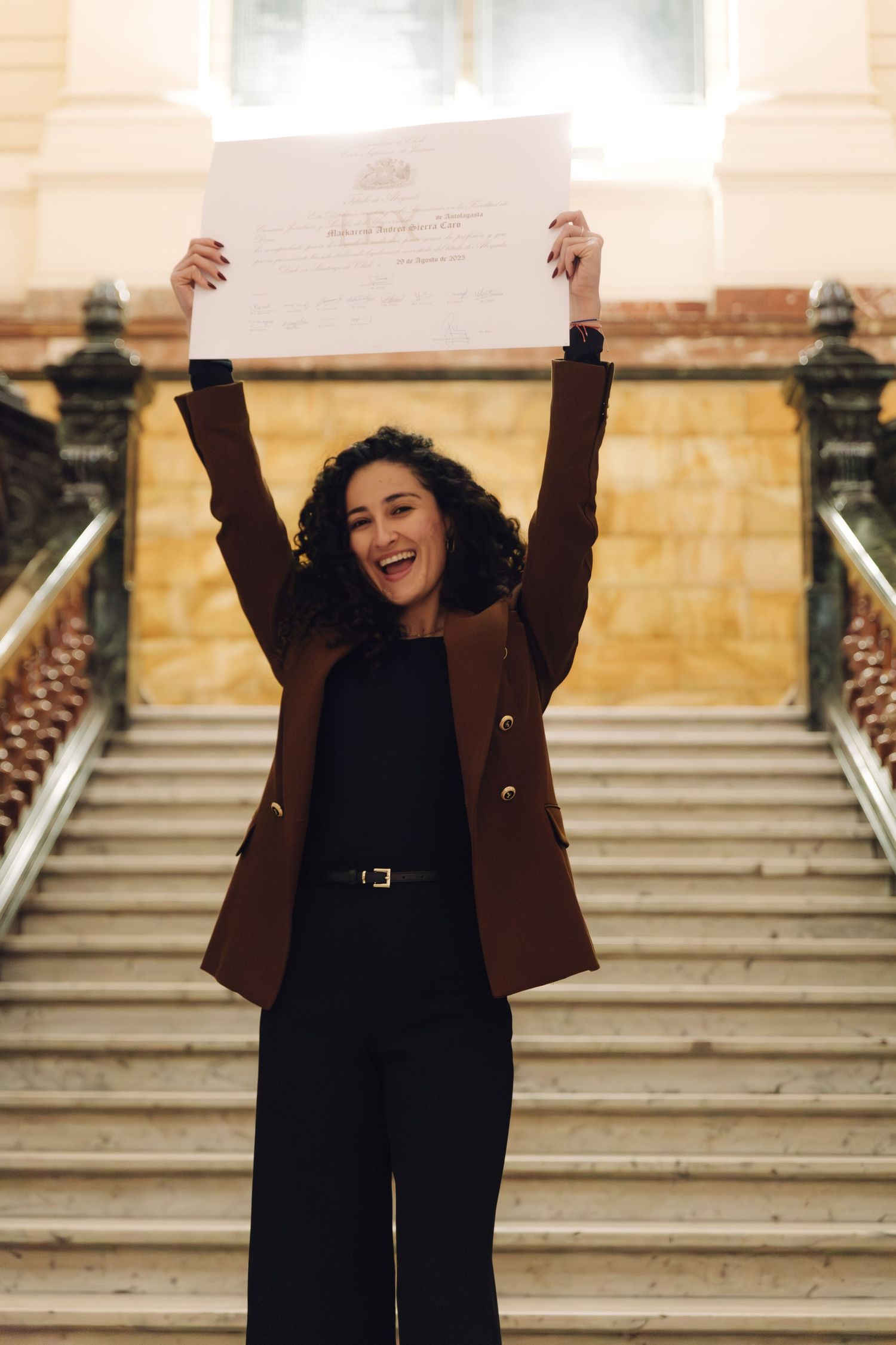 Excited woman raising diploma above her head in triumph on a staircase.