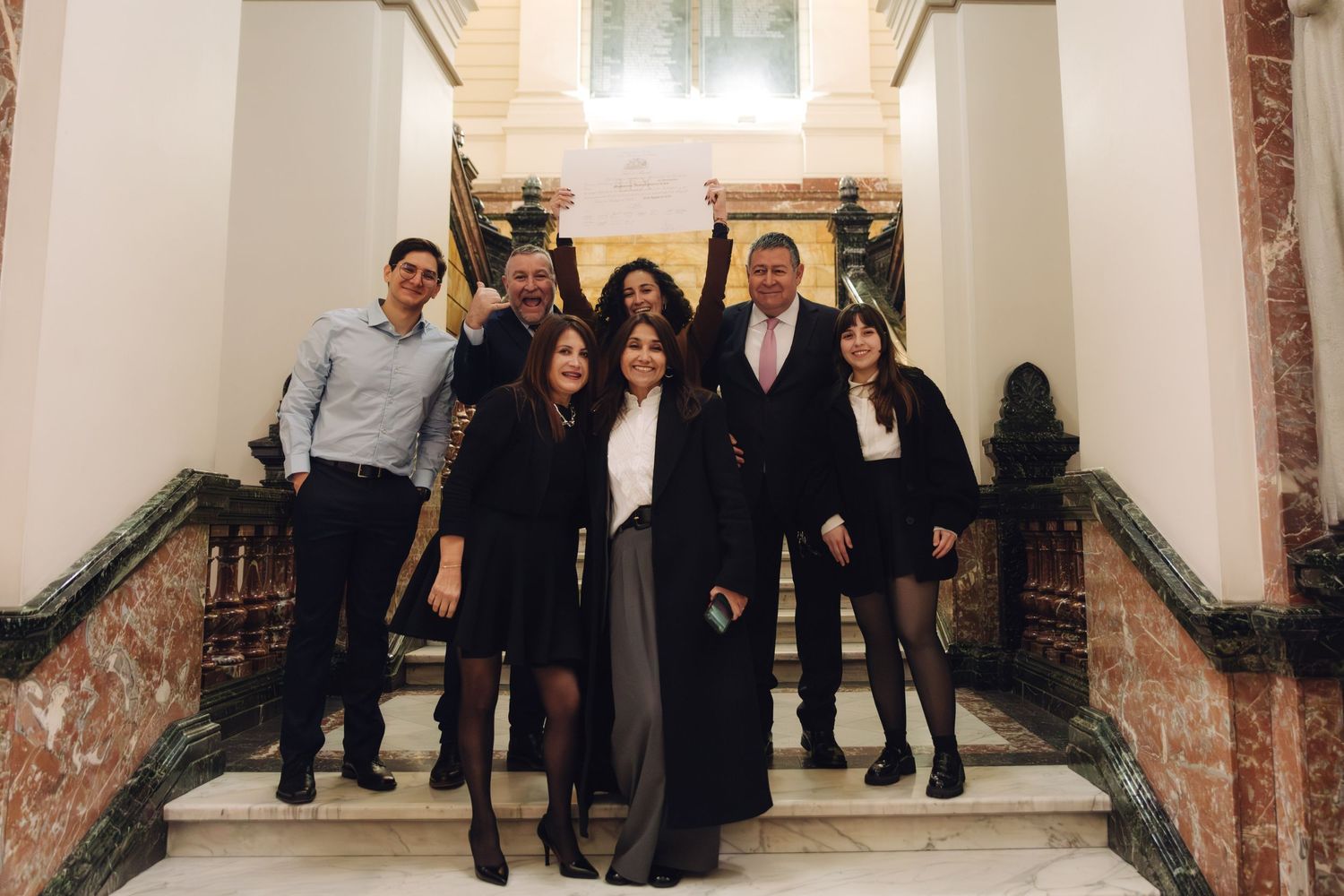Group of eight professionals posing on elegant marble staircase in formal attire at an upscale venue.