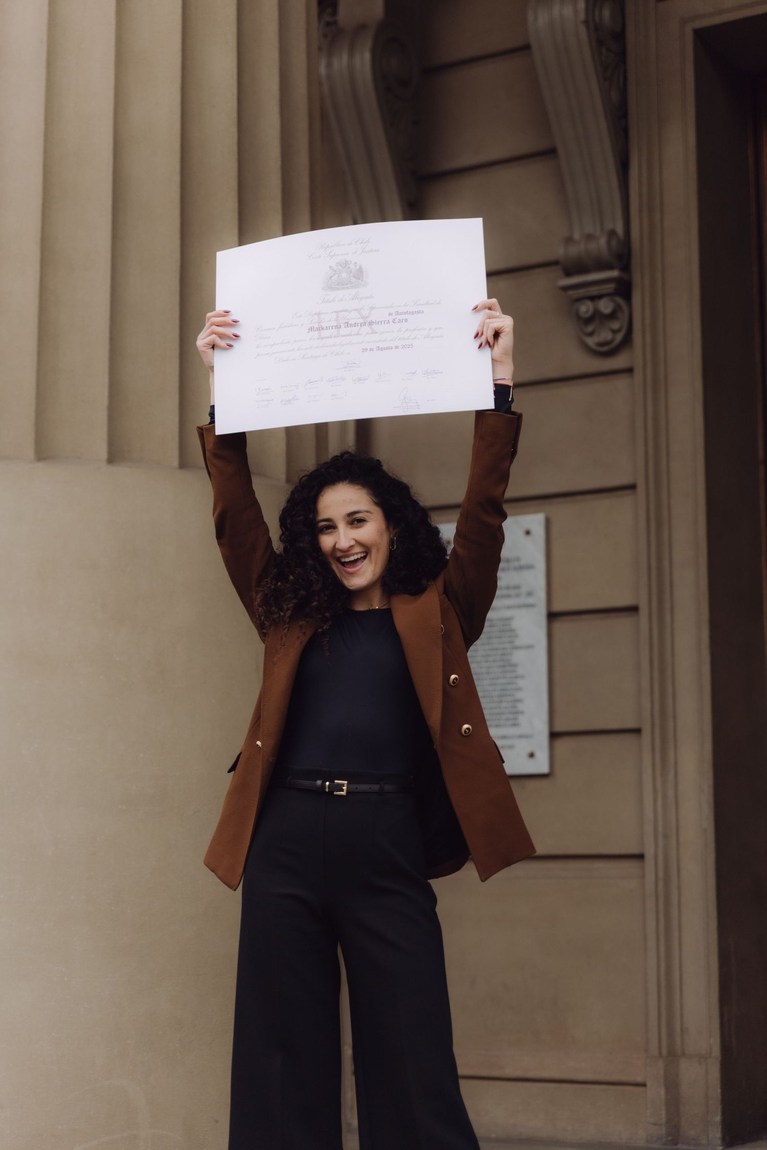Excited young woman raising diploma certificate above head celebrating graduation outside building.
