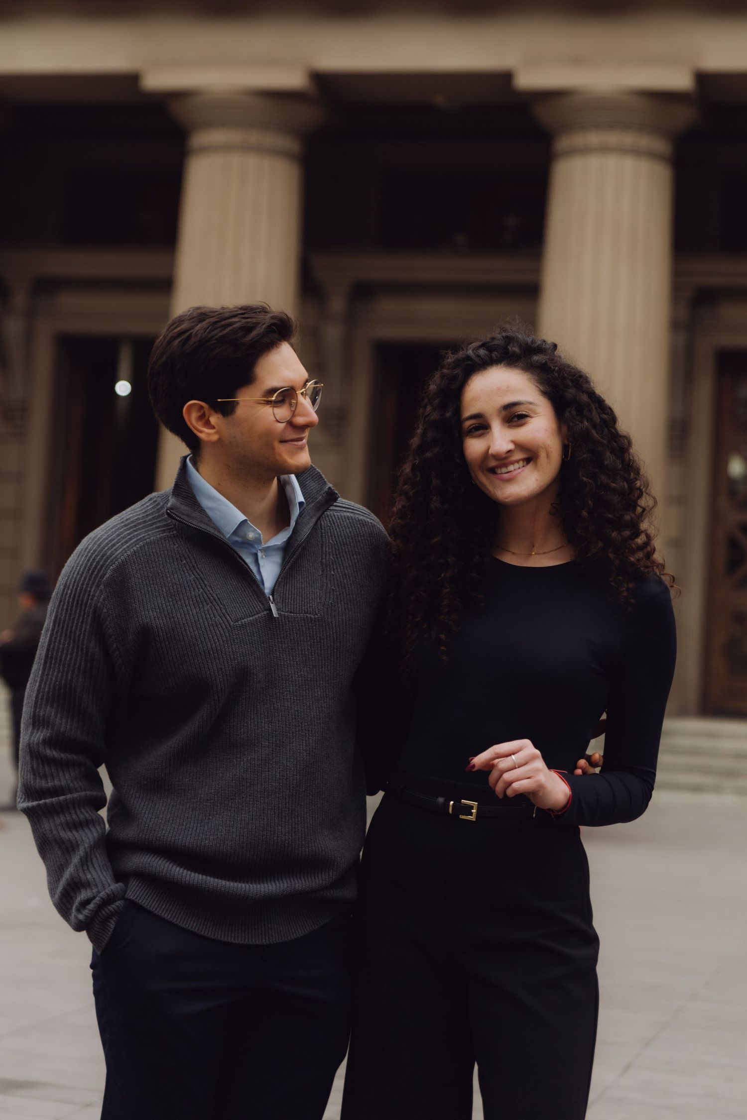 Smiling couple stands together in front of classical columned building facade.