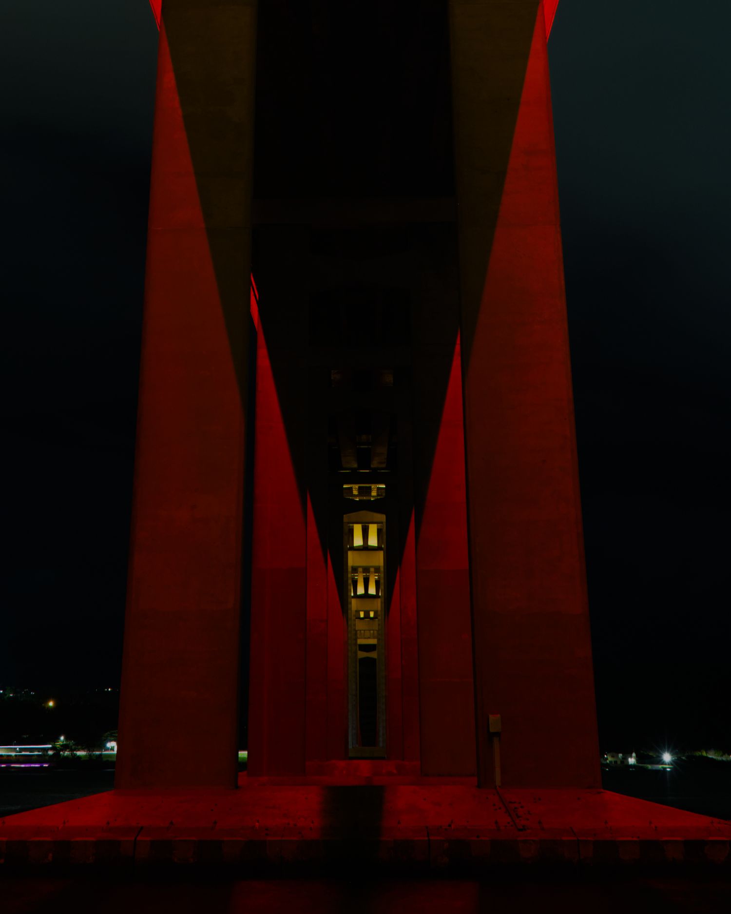 Red-lit bridge columns frame a glowing historic tower at night, creating dramatic symmetry.