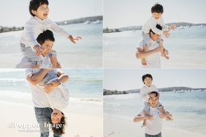 Father and son playfully posing on a sunny beach, with the boy riding on his dad's shoulders and back.