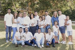 Large family group portrait outdoors on green lawn, wearing coordinated white tops and jeans, smiling together.