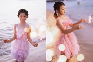 Young girl in pink tulle dress holding sparklers on a beach at sunset, creating a magical, dreamy atmosphere.