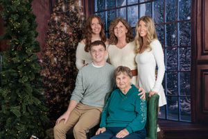 Five-generation family Christmas portrait posed near a decorated holiday tree in festive attire.