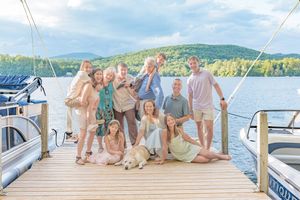 Large family group smiling together on a boat dock with a lake and mountains behind them.