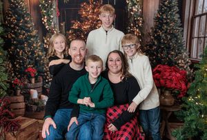 Family of five Christmas portrait with decorated trees and holiday decor backdrop.