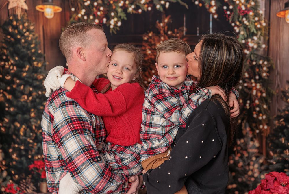 A family of four in matching plaid pajamas shares kisses during a festive Christmas photo session.