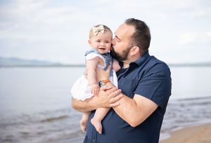 Loving father kissing his baby daughter on the cheek while standing near a calm lake shore. Ellacoya State Park, Gilford NH.
