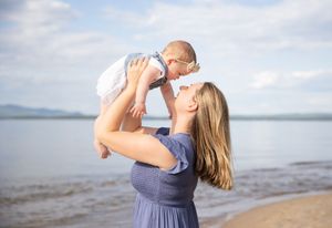 Mother lifting baby at beach, sharing a tender kiss moment with ocean backdrop. Ellacoya State Park, Gilford NH.