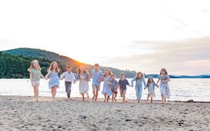 Group of children holding hands running on beach at sunset with mountain views. Ellacoya State Park, Gilford NH.