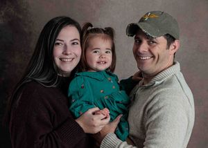 Happy family studio portrait with parents holding smiling toddler girl in green dress.
