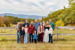 Extended family portrait in autumn field with colorful fall foliage and mountains.