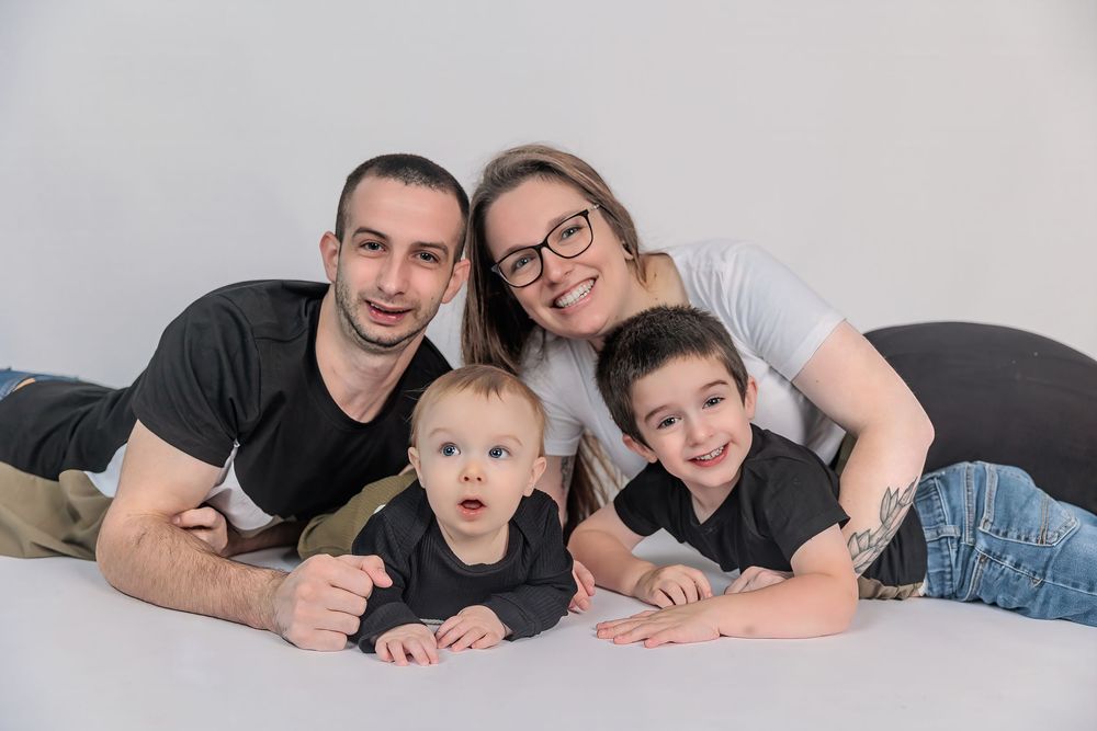 Young family of four posing together on white background, including two boys and smiling parents.
