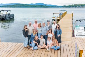Large family group photo on a wooden lake dock with boats and mountains in the background. Weirs Beach Laconia NH.