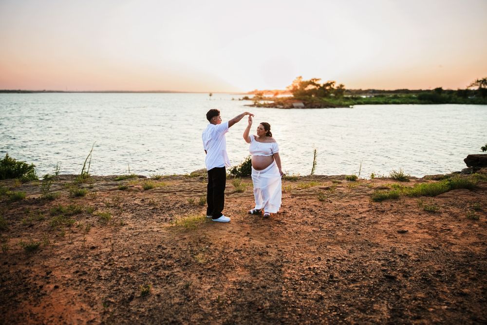 Couple in white dancing at sunset by the water on red earth ground.