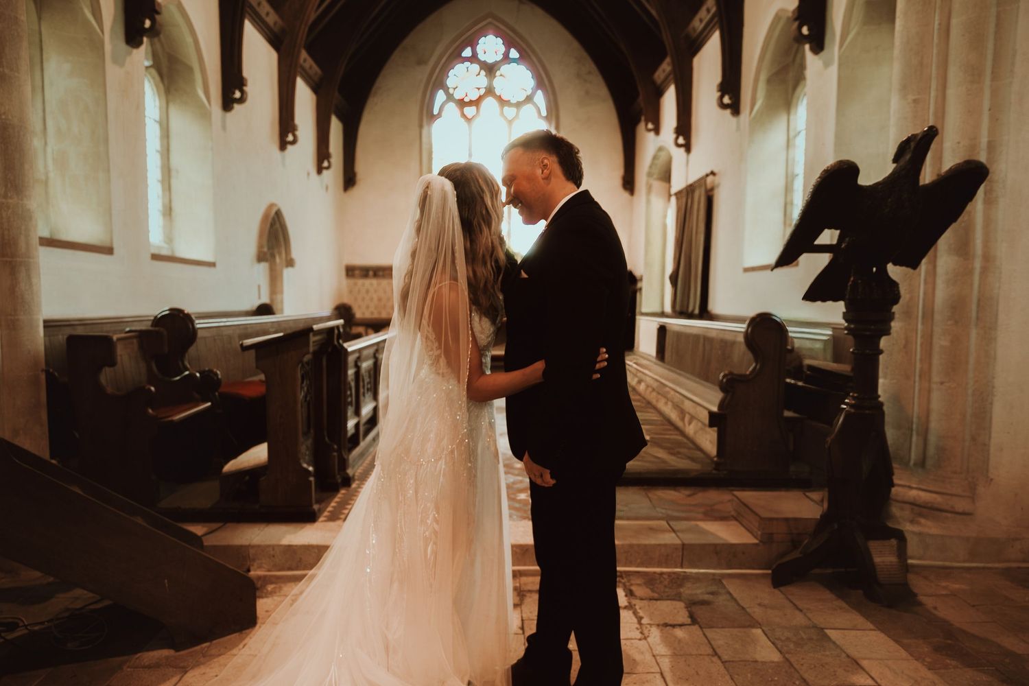 Bride and groom share a romantic moment inside a historic church with gothic stained glass windows on their wedding day.