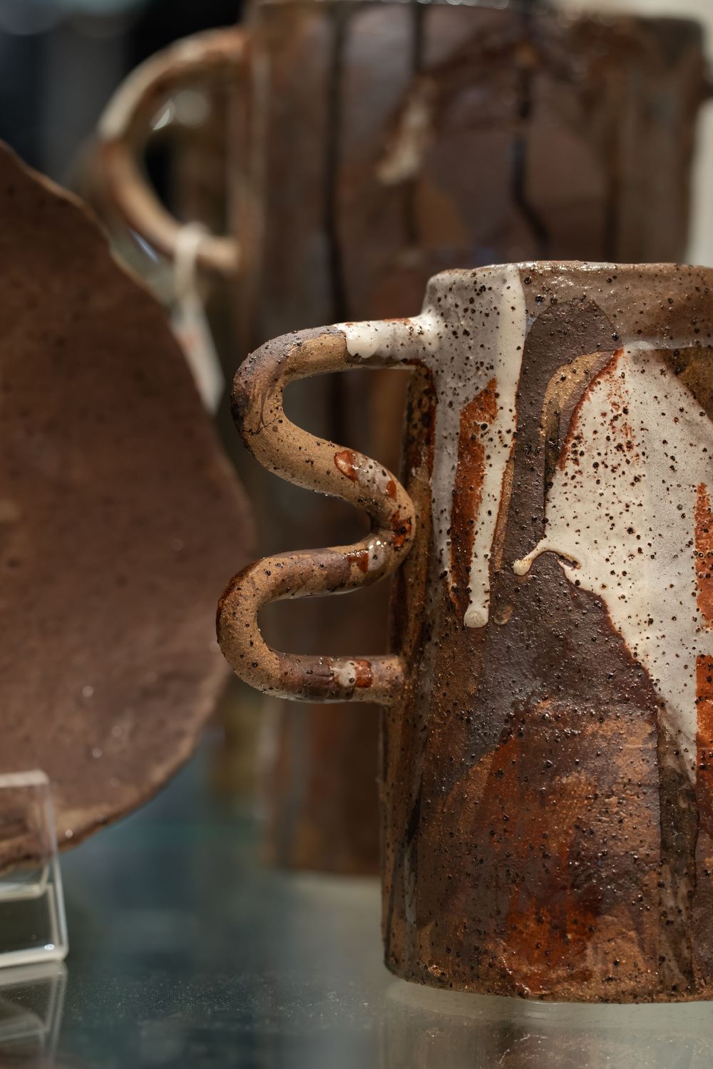 Rustic handmade ceramic mugs with brown and white drip glaze on a reflective surface.