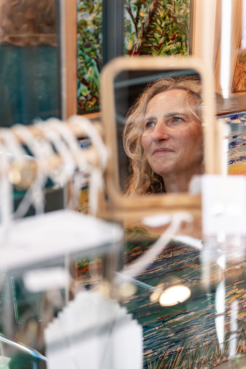 Woman browsing colorful artwork and jewelry displays at an art gallery or craft fair.