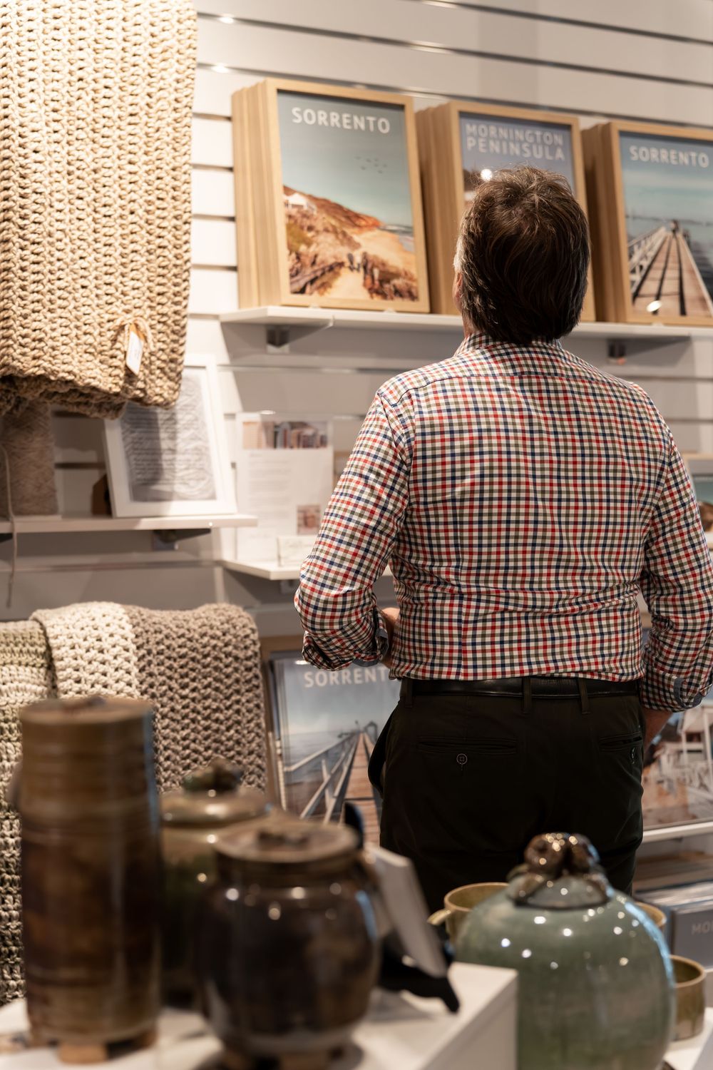 Man browsing Sorrento Peninsula travel prints and ceramic pottery in a coastal lifestyle gift shop.