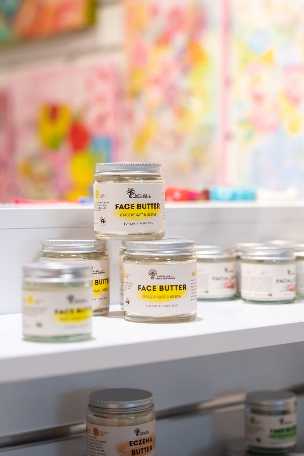 Jars of face butter and eczema butter skincare products displayed on a white shelf in a bright boutique store.