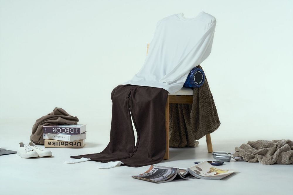 White t-shirt and brown pants draped over wooden chair surrounded by books, magazines, and casual accessories.