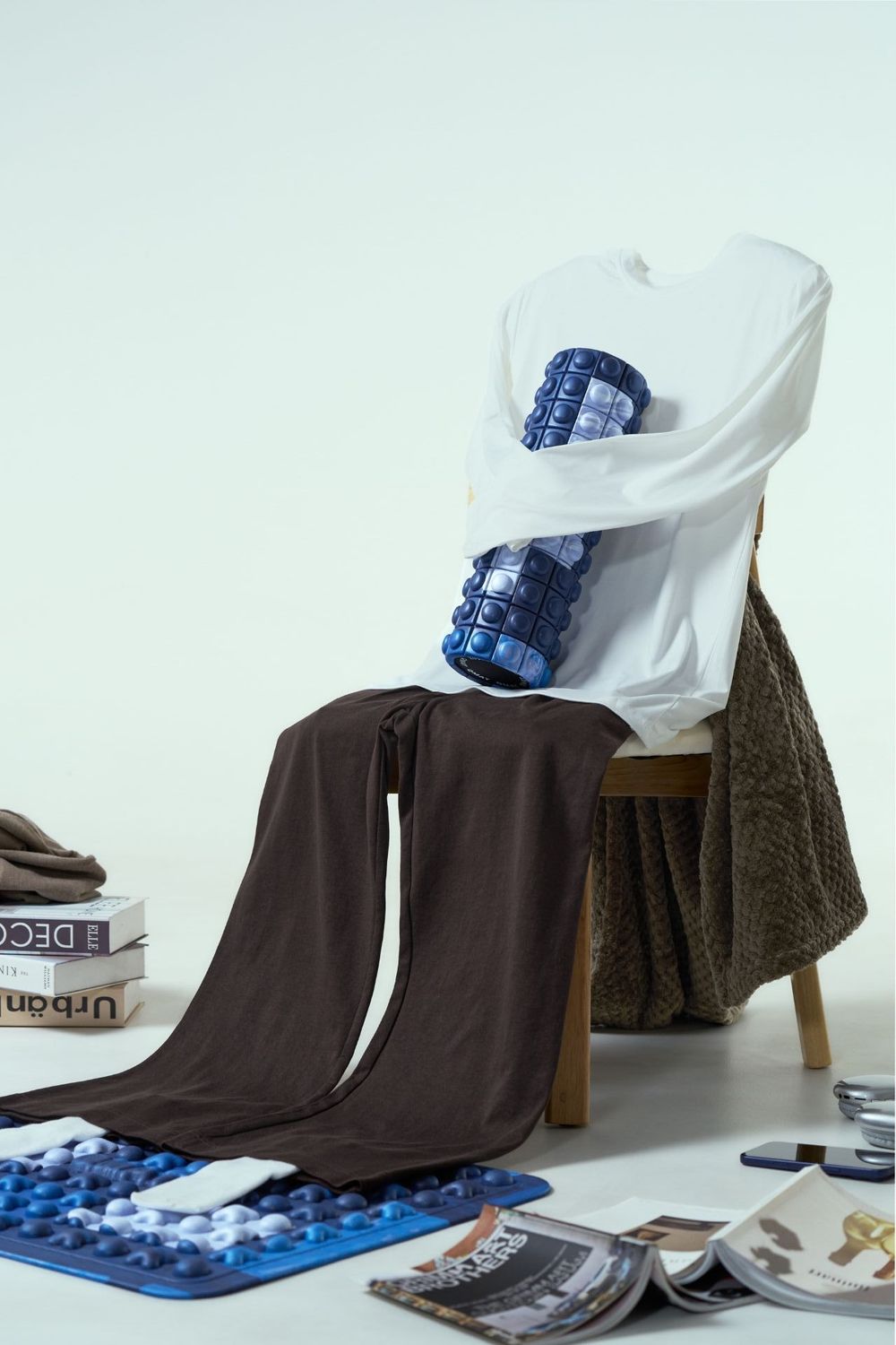 White long-sleeve shirt with blue foam roller on chair, surrounded by books, magazines, and brown blanket.