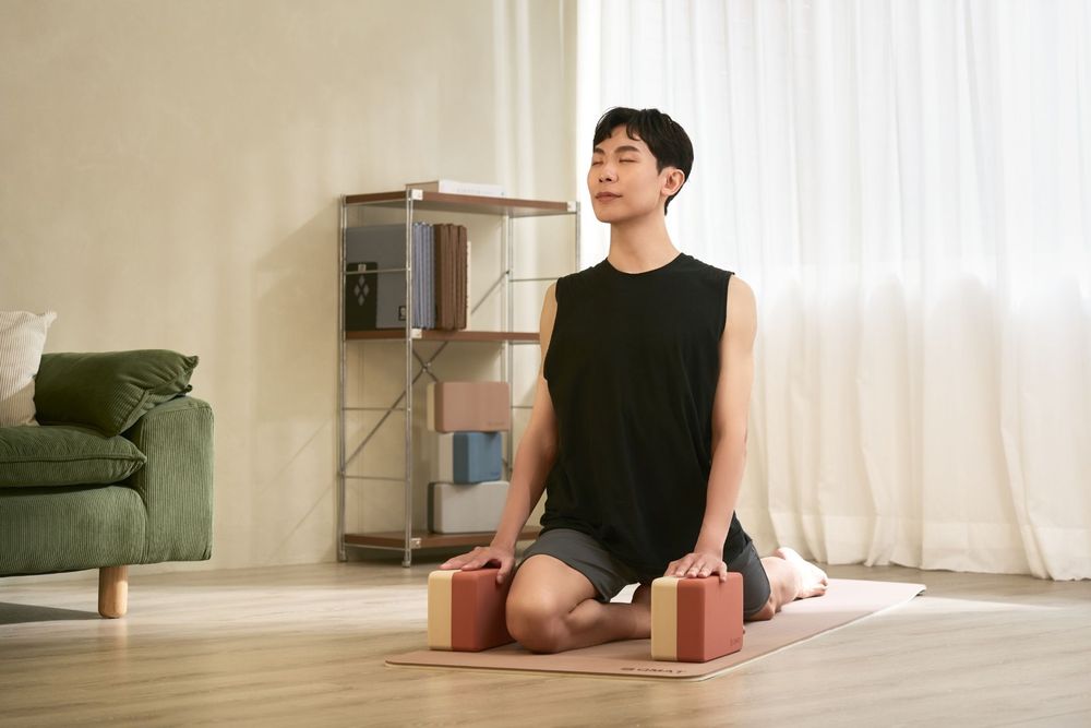 Man meditating on yoga mat with blocks in bright minimalist living room, practicing mindfulness yoga.