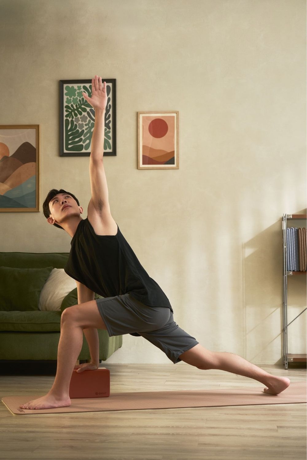 Man practicing yoga in a side angle pose on a mat at home with artwork on the wall behind him.