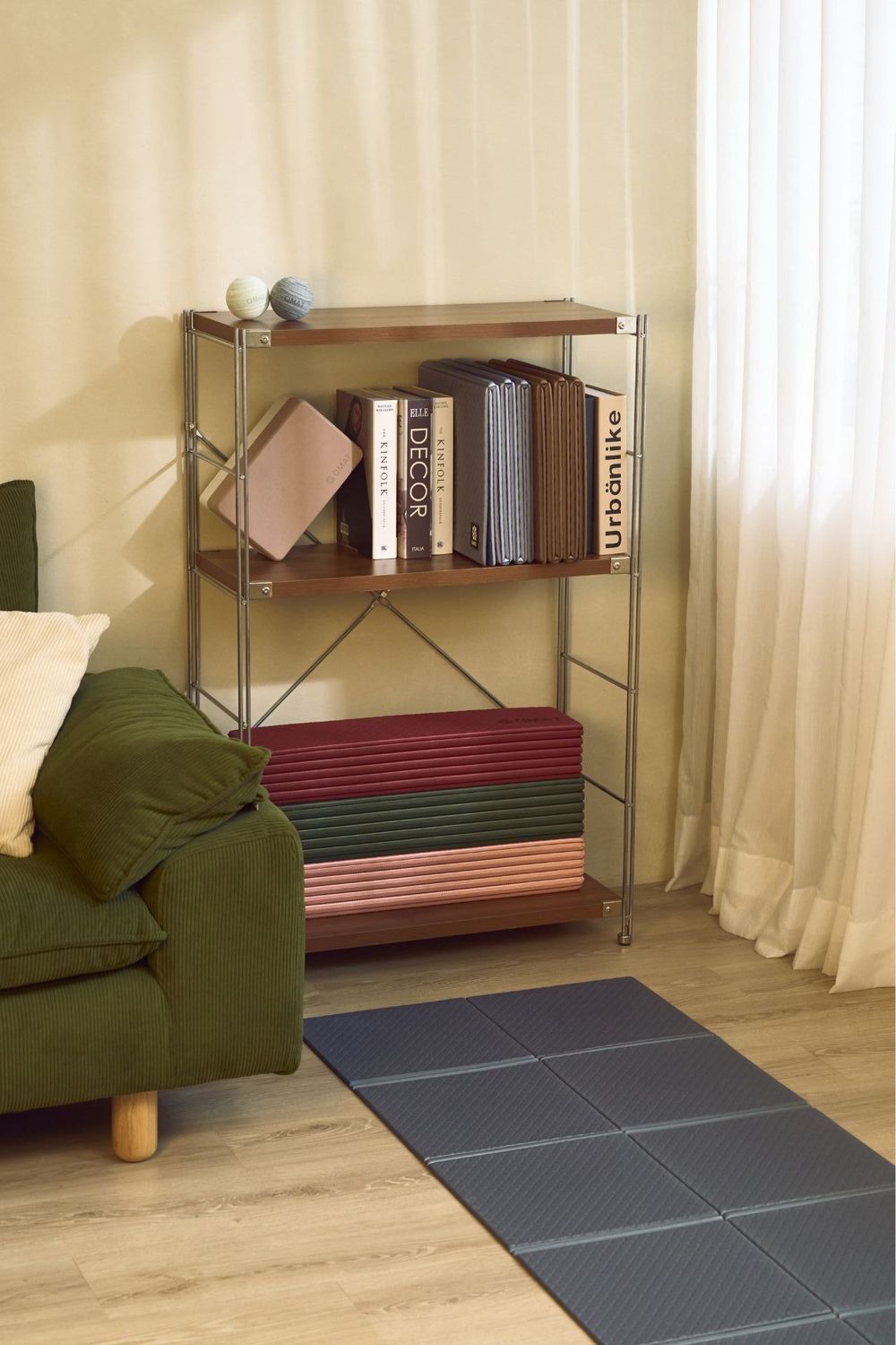 Metal shelving unit with wooden shelves displaying books and colorful folded mats in a modern living room.