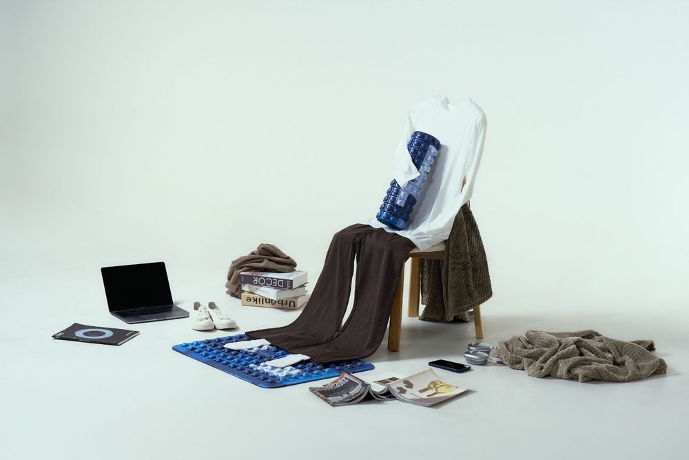 A wooden chair surrounded by clothing, a laptop, shoes, and accessories arranged on a white background.