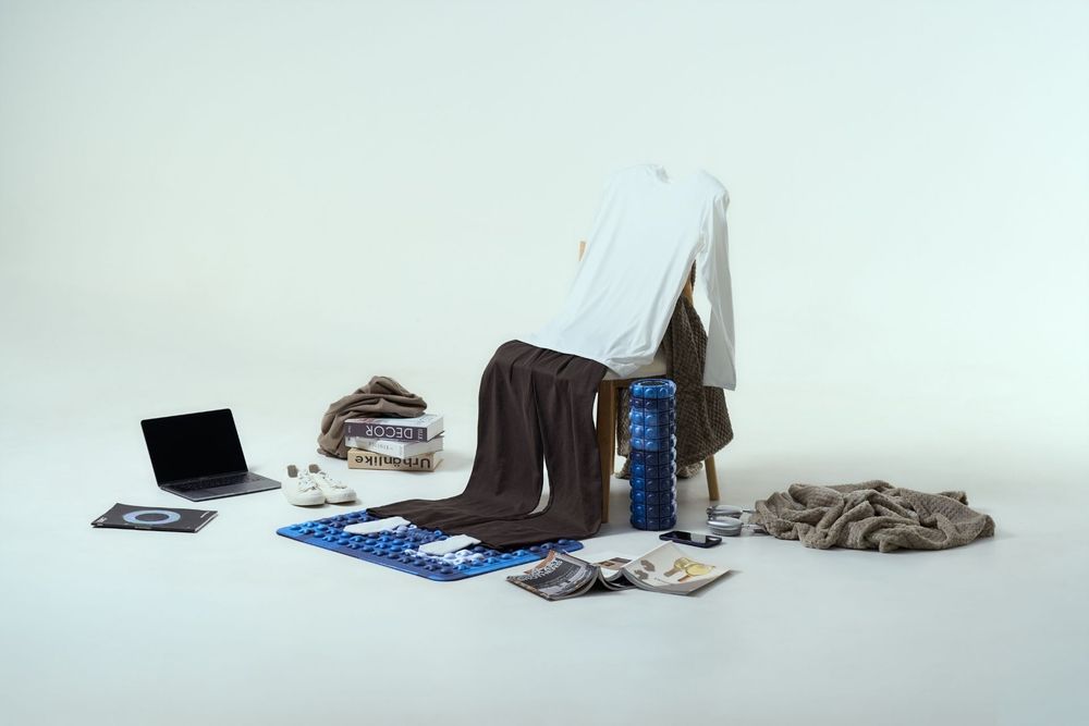 White shirt on chair surrounded by laptop, brown blanket, blue foam roller, books, and scattered accessories.