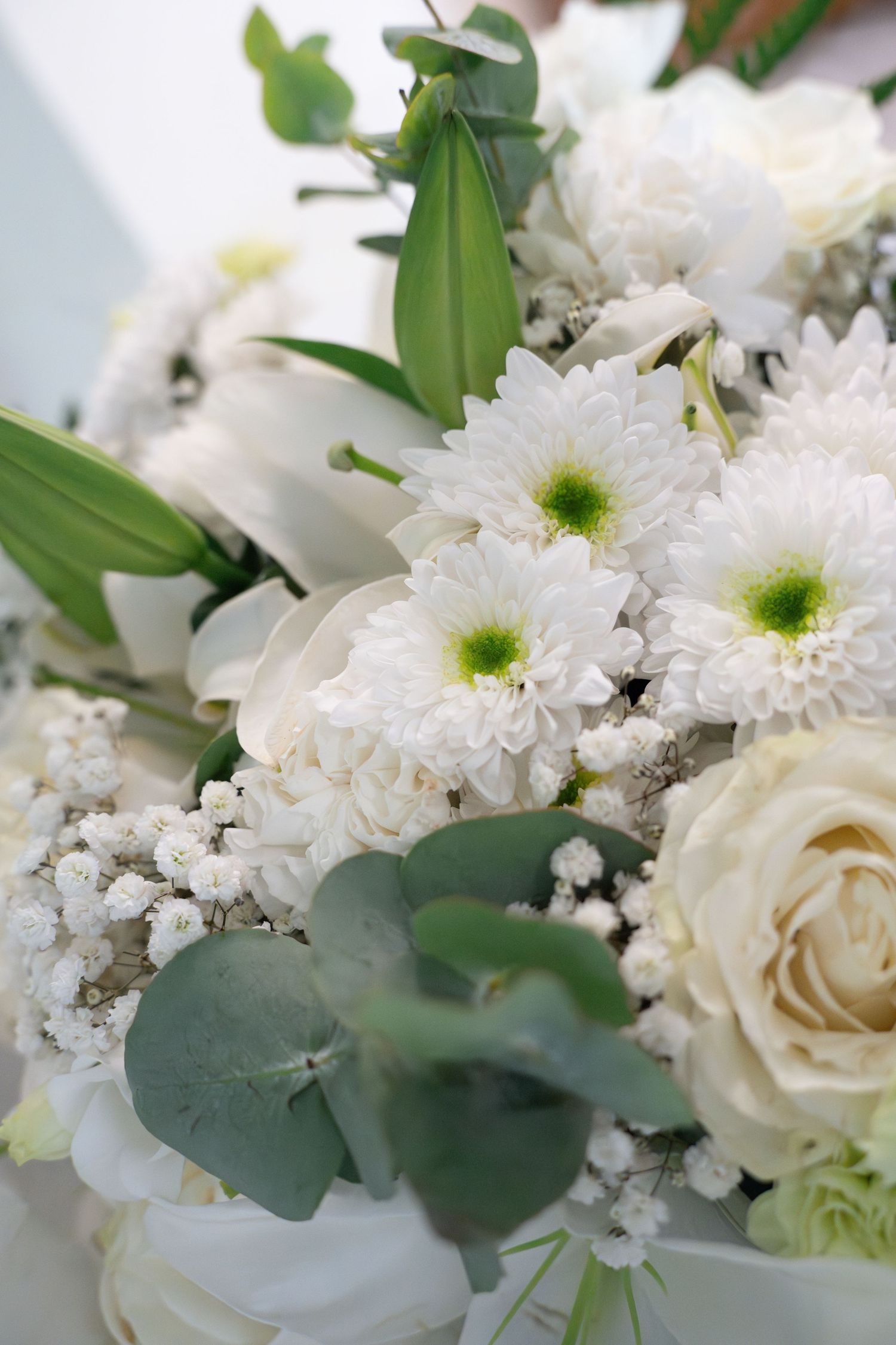 Elegant white floral arrangement with roses, chrysanthemums, baby's breath, and eucalyptus leaves for a wedding.