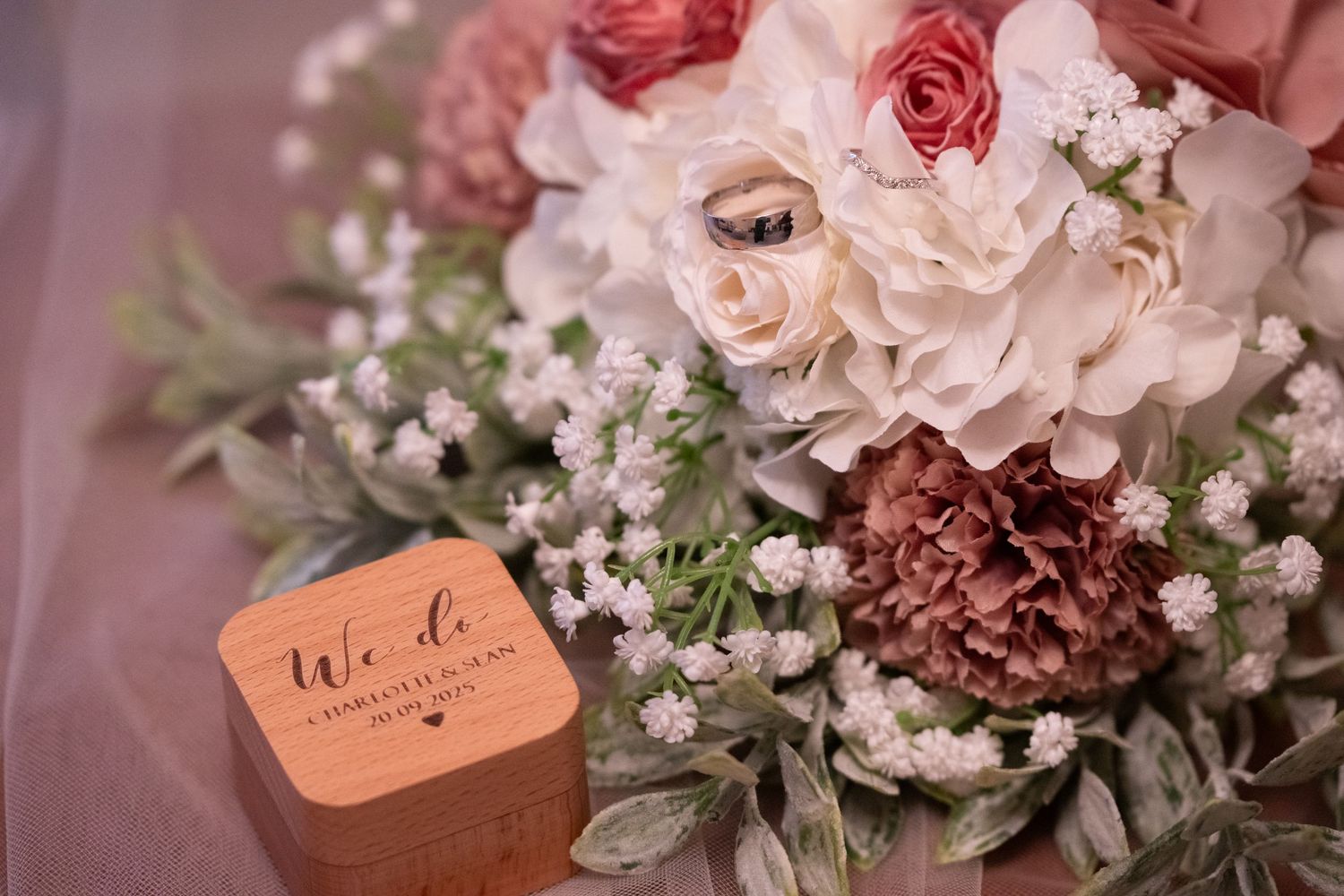 Elegant wedding bouquet with blush roses and a wooden "We Do" ring box on a soft pink background.