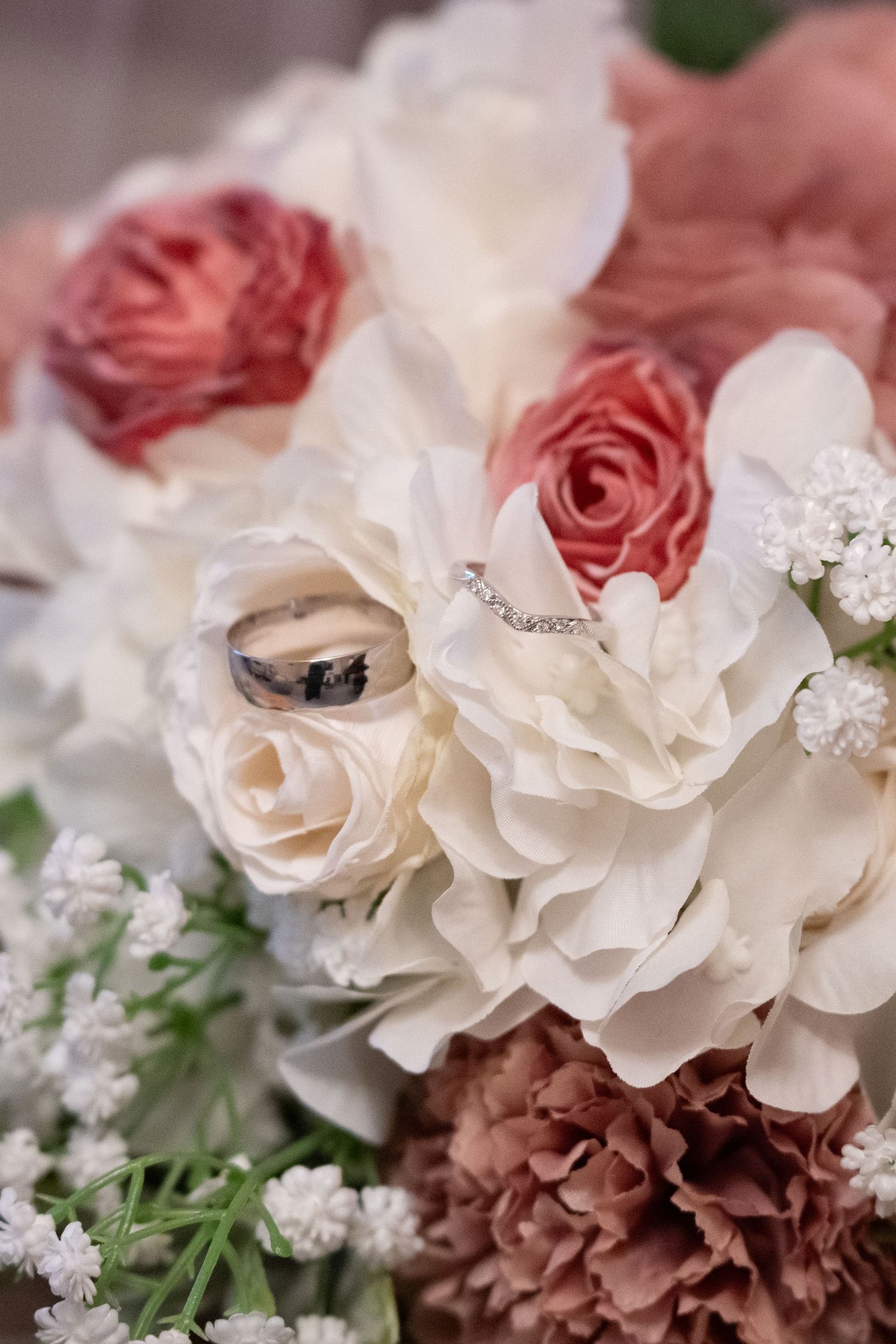 Wedding rings resting on a bridal bouquet of white and pink roses with baby's breath.