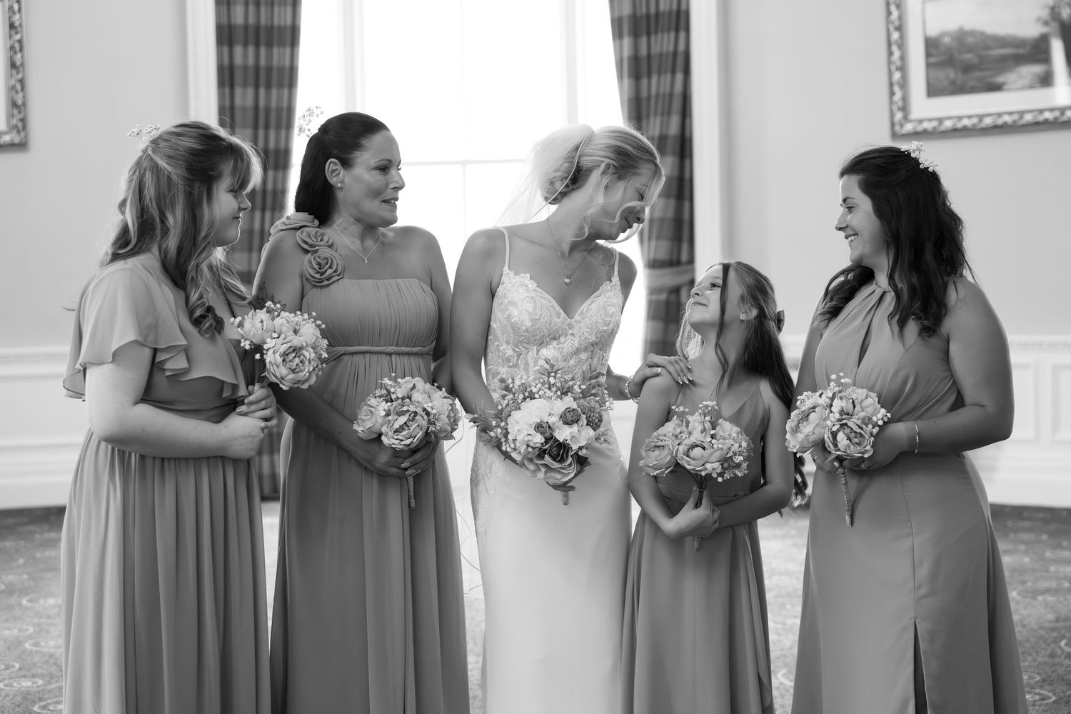 Bride in white gown with four bridesmaids in matching dresses holding bouquets, black and white wedding photo.
