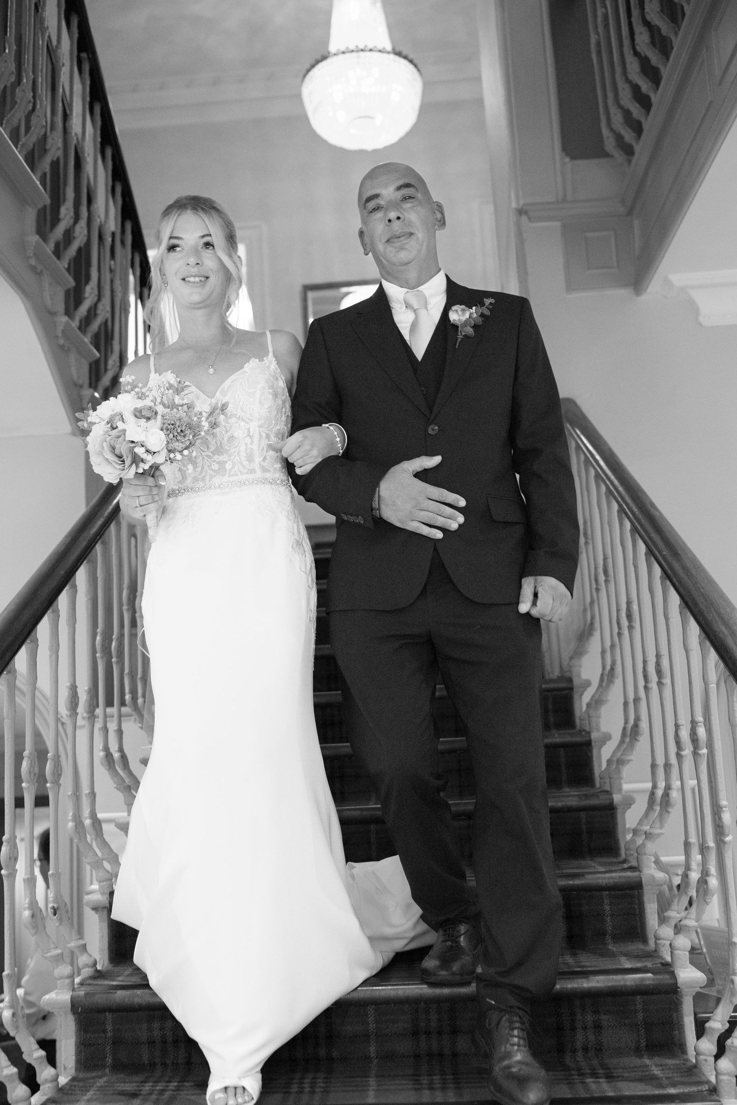 Bride and groom descending a grand staircase together in black and white wedding photo.