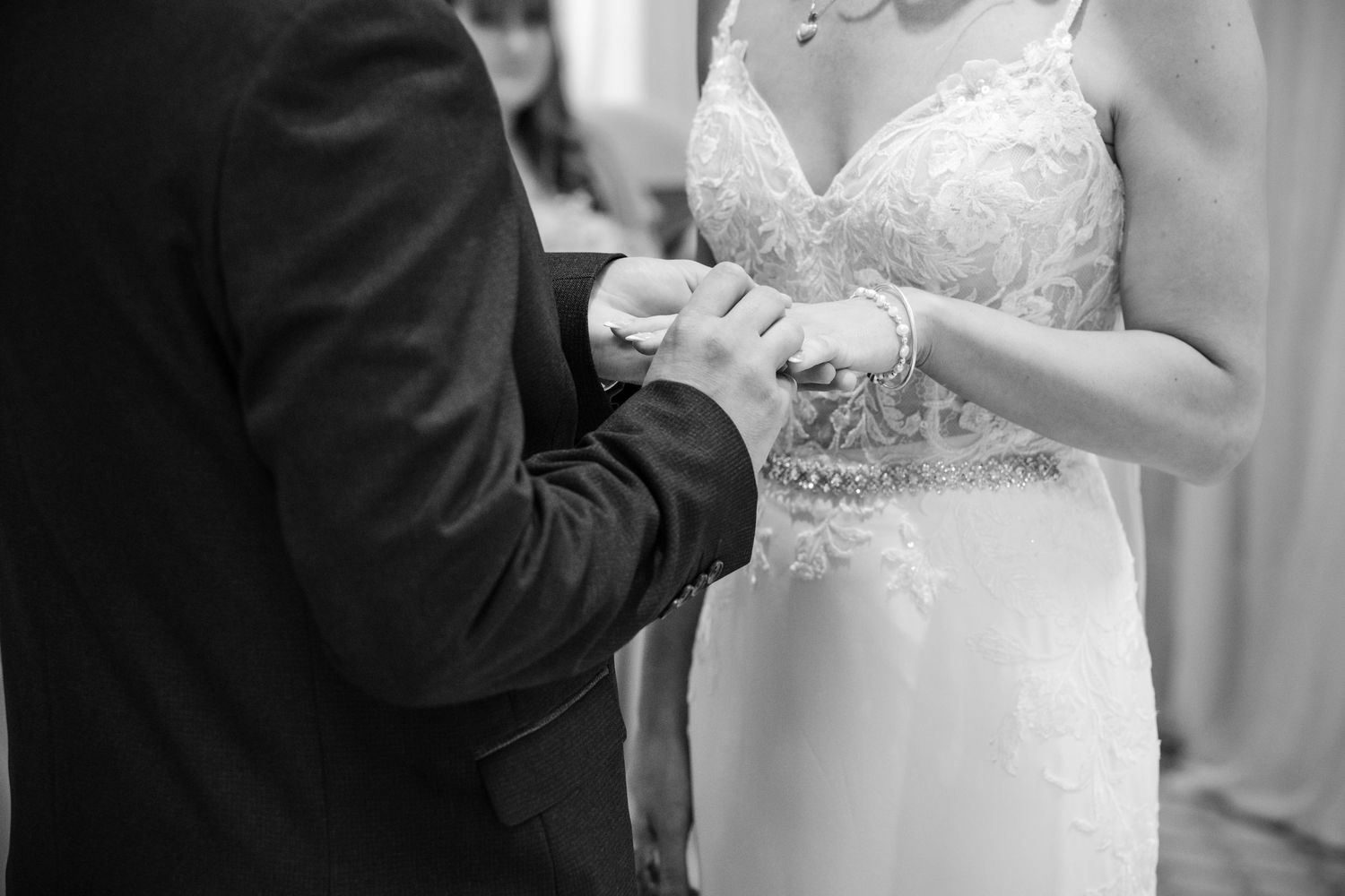 Black and white photo of bride and groom exchanging rings during wedding ceremony.