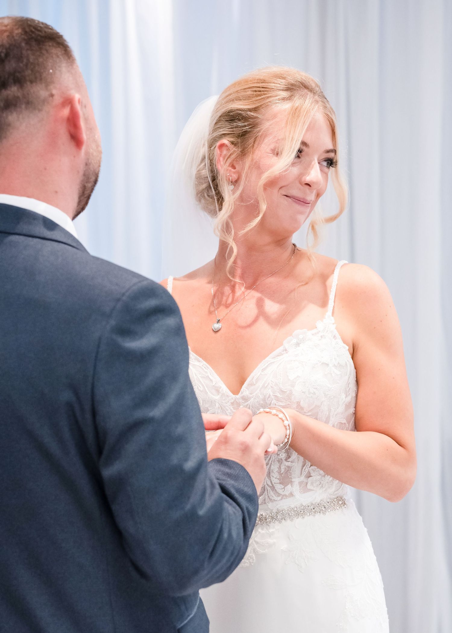 Emotional bride holding grooms hands during wedding ceremony vows in decorated venue.