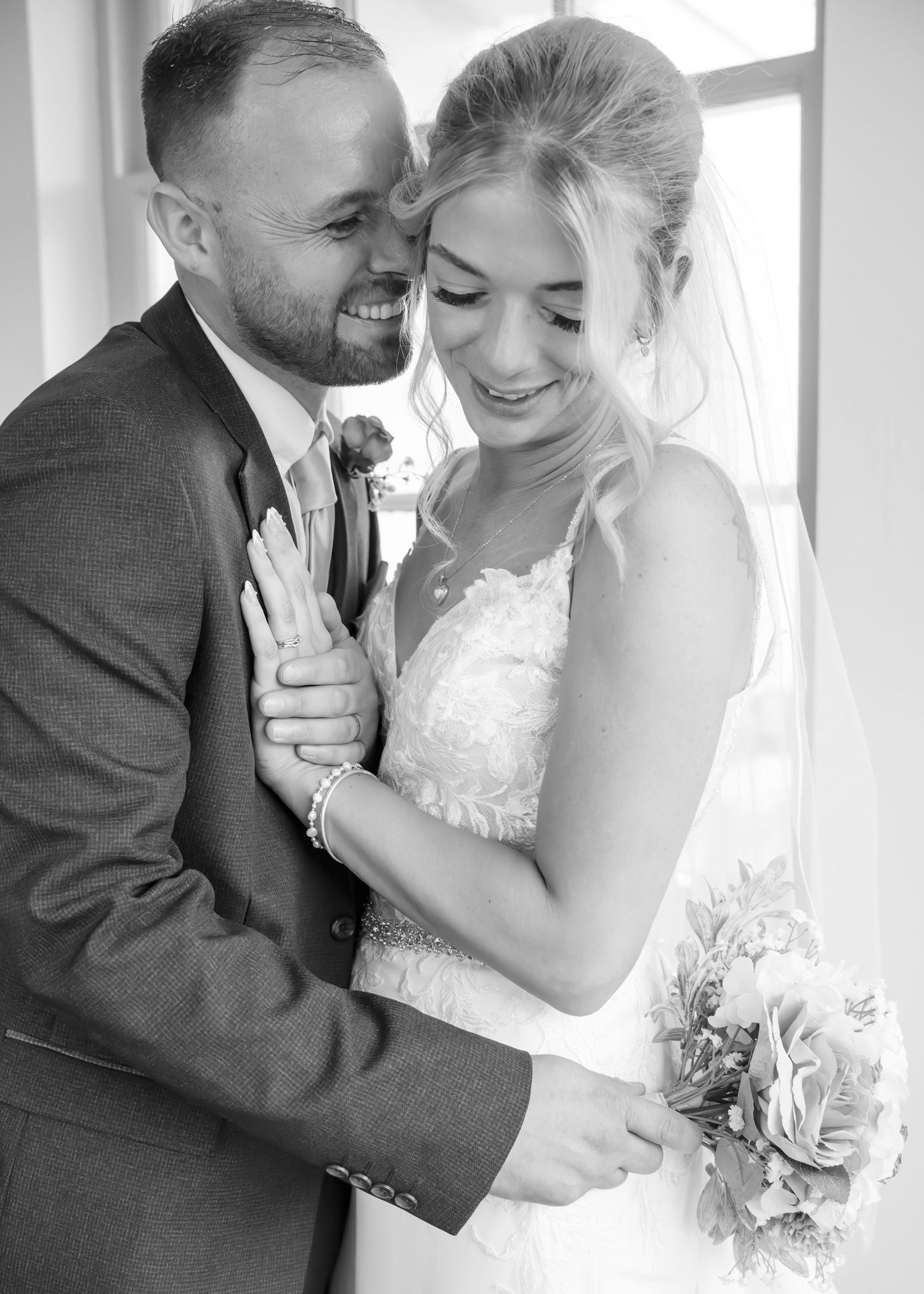 Black and white photo of smiling bride and groom embracing tenderly before their wedding ceremony.