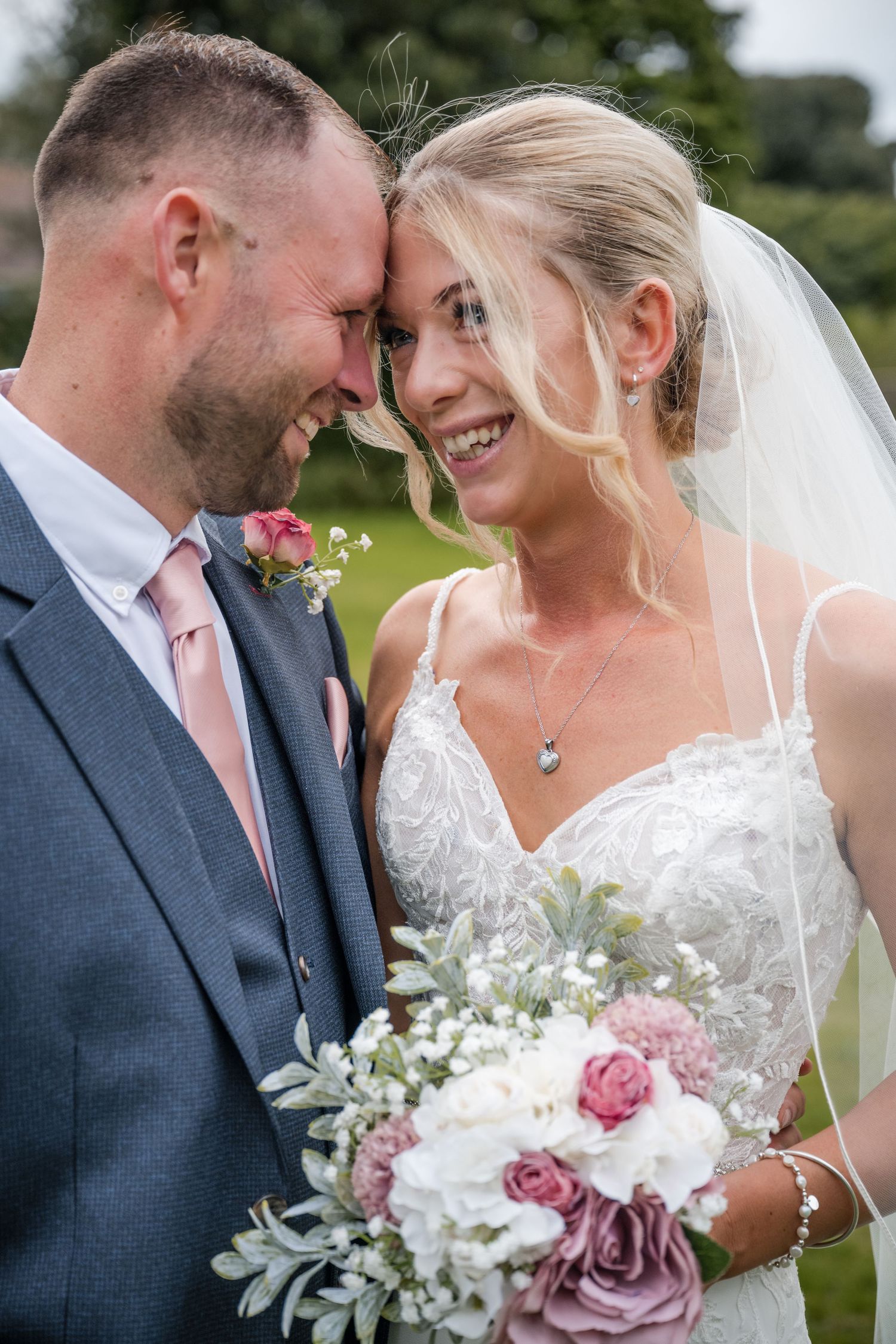 Smiling bride and groom sharing an intimate forehead touch moment with floral bouquet.