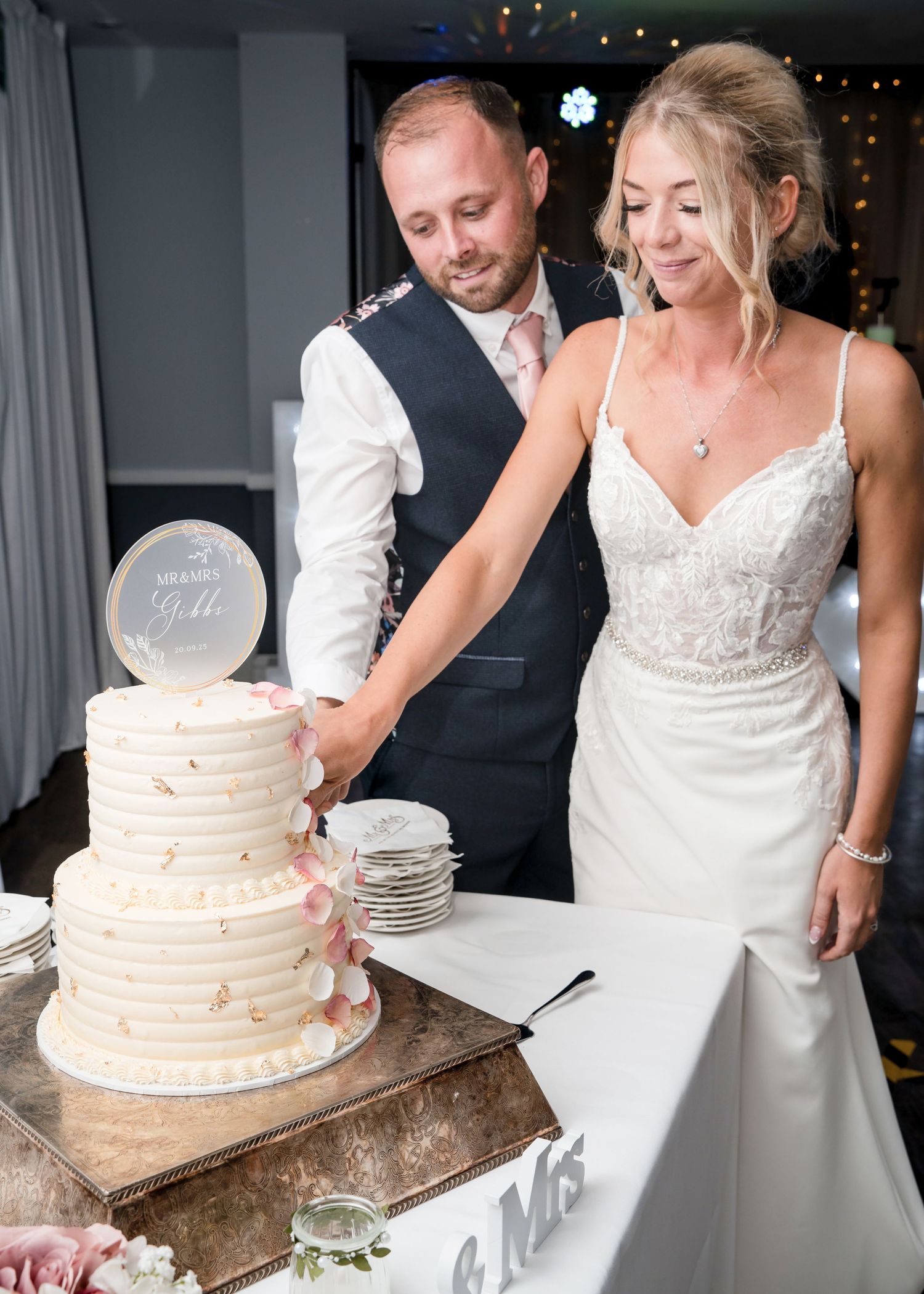 Bride and groom cutting their white tiered wedding cake together at their wedding reception.