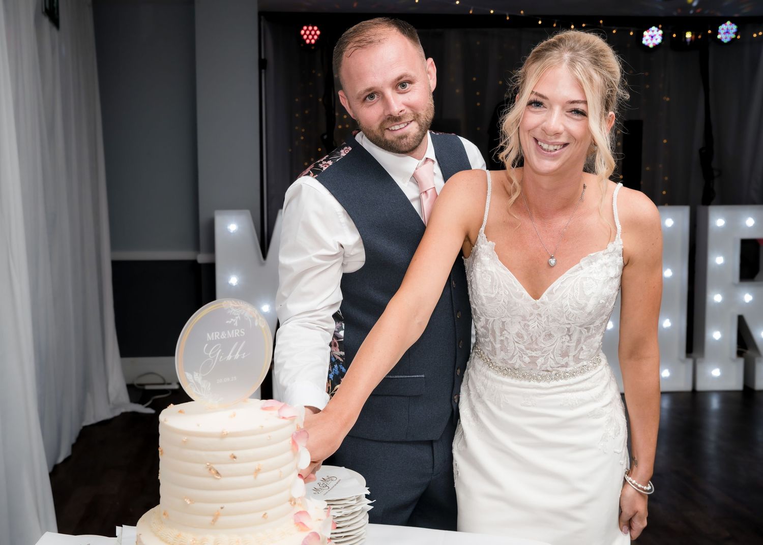 Smiling bride and groom cutting their white wedding cake together at their wedding reception.