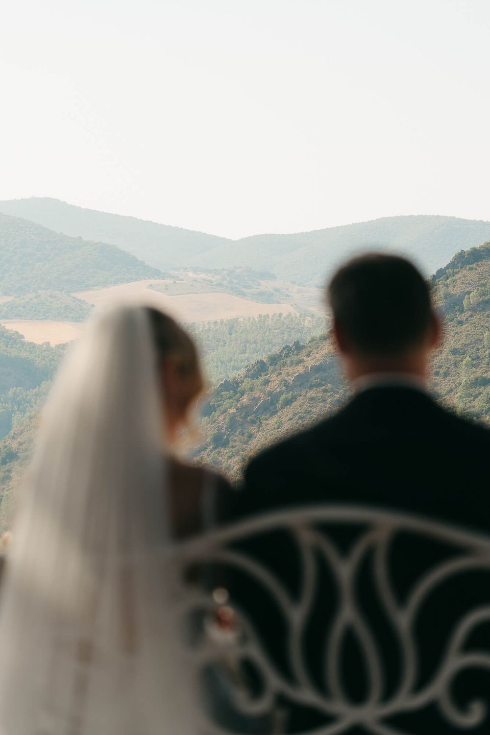 Bride and groom stand together on a balcony overlooking lush green mountains on their wedding day.