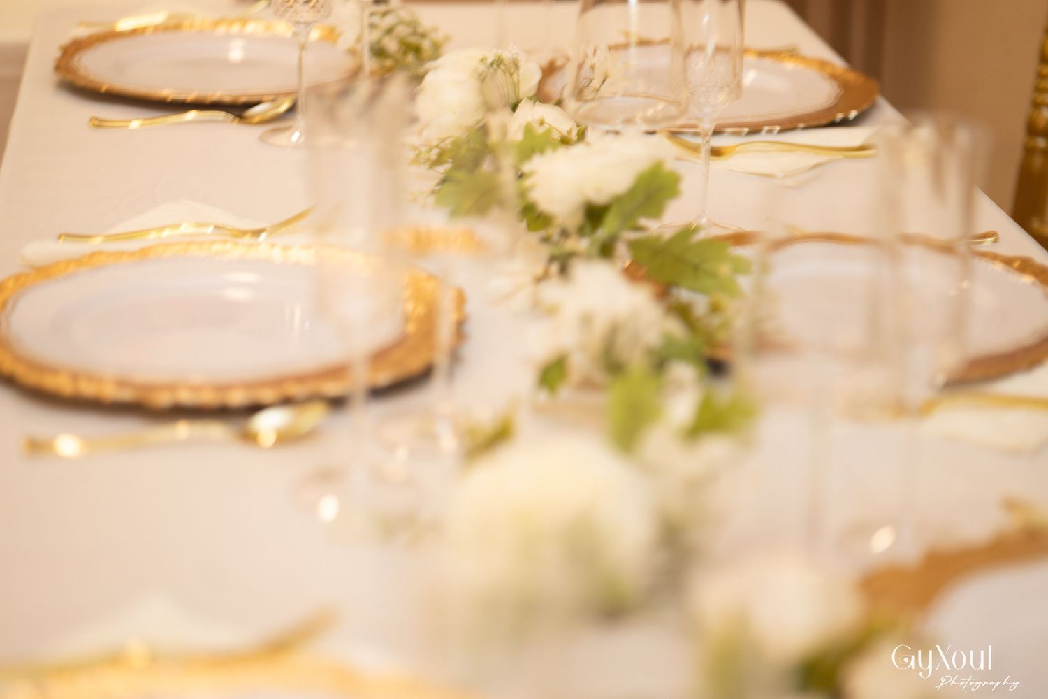 Elegant wedding table setting with gold charger plates, white roses, crystal glassware, and gold cutlery on ivory linen.