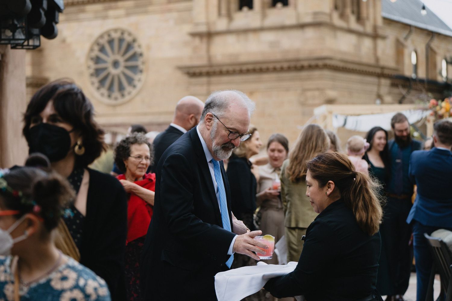 Man in suit signing autograph outdoors near historic cathedral with crowd of people gathered around him.